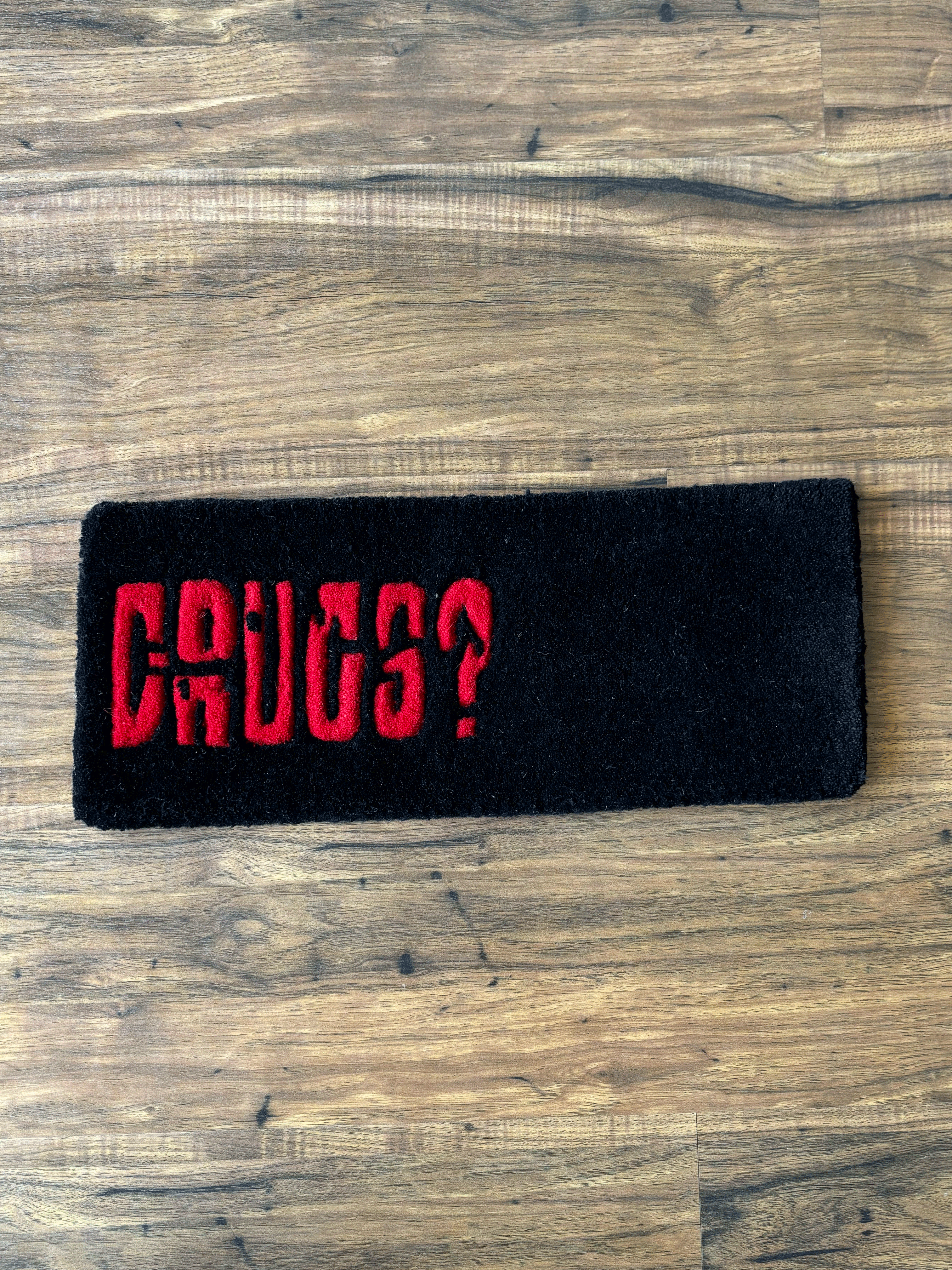 A black woolen keyboard rug with the word 'DURGS?' printed in red, placed on a wooden floor.
